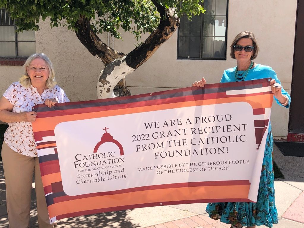 Two women smiling and holding a large banner announcing a 2022 grant from the Catholic Foundation.
