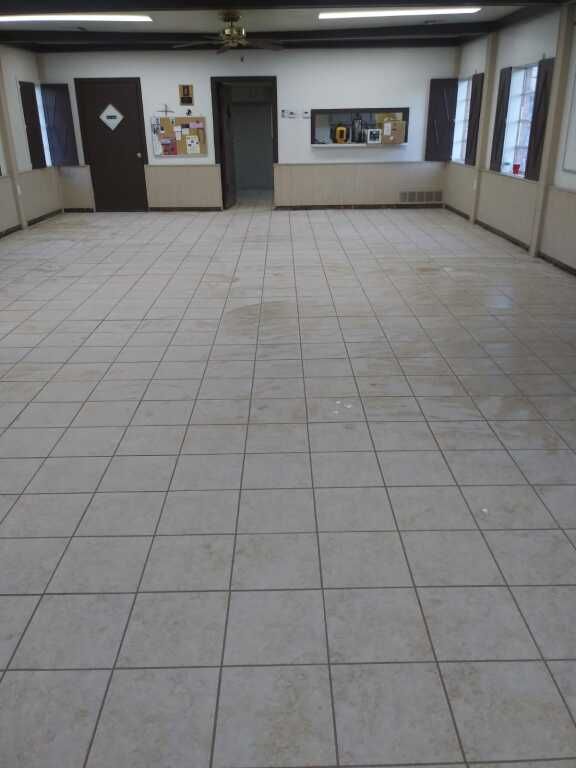 Spacious room with beige tiled flooring, neutral-colored walls, and fluorescent ceiling lights.