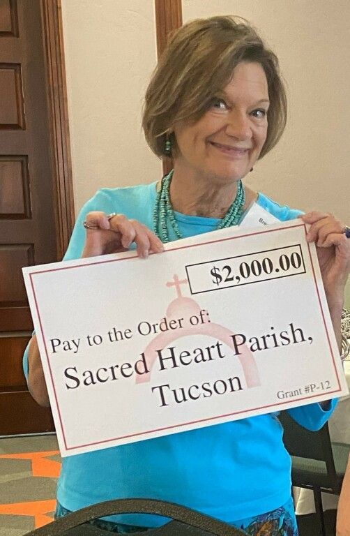 Woman smiling while holding a large check for $2,000 made out to Sacred Heart Parish, Tucson.