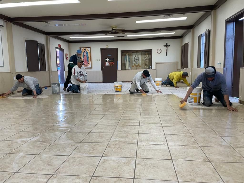 Five men kneel on a tiled floor, working diligently on the tiles with sponges and buckets.