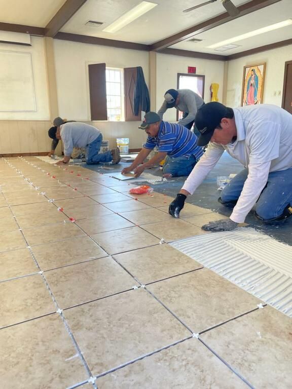 Four workers are installing tiles on a large floor in a room. 