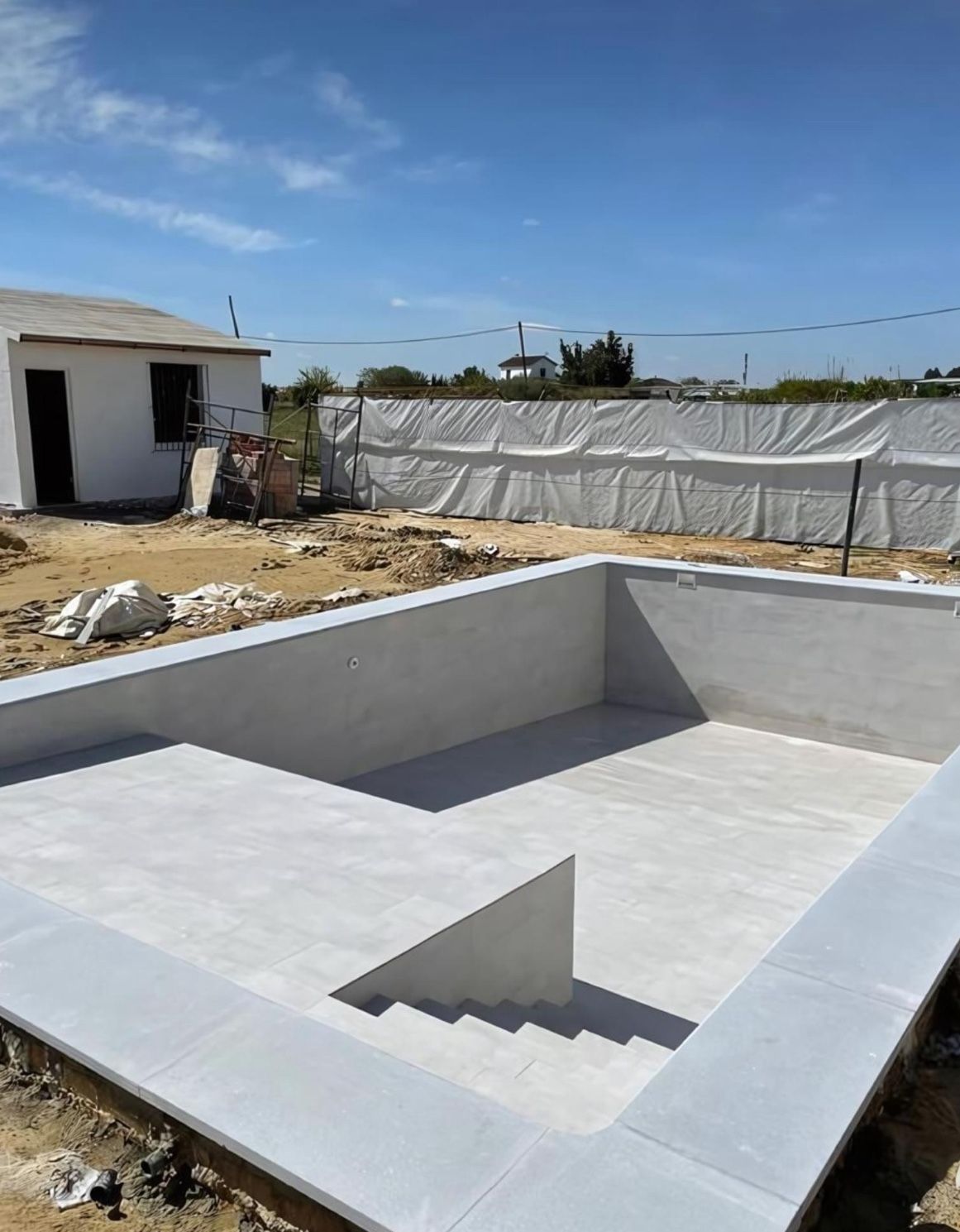 Une piscine est en cours de construction dans une cour arrière avec une maison en arrière-plan.