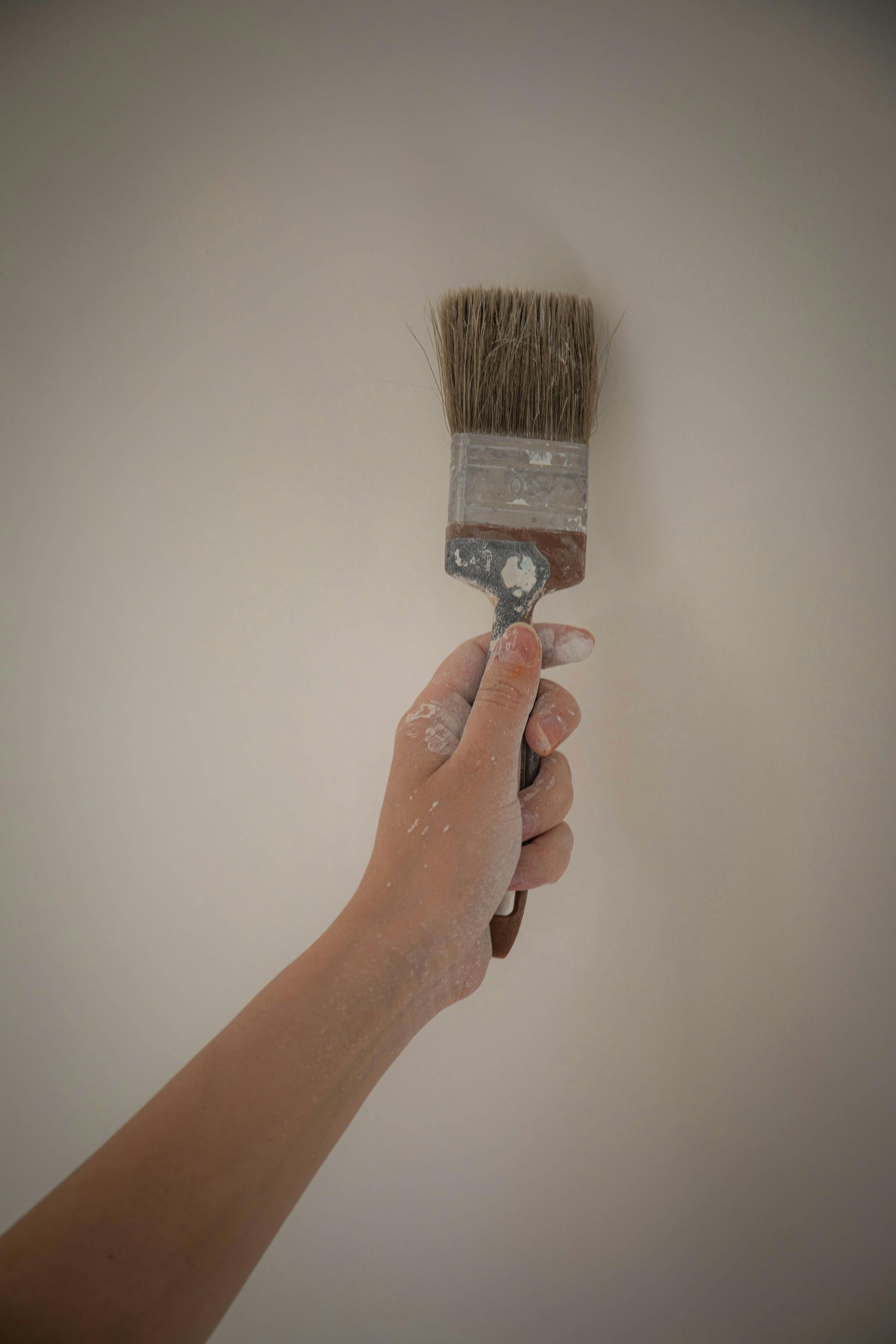 Hand holding a paintbrush against a blank beige wall