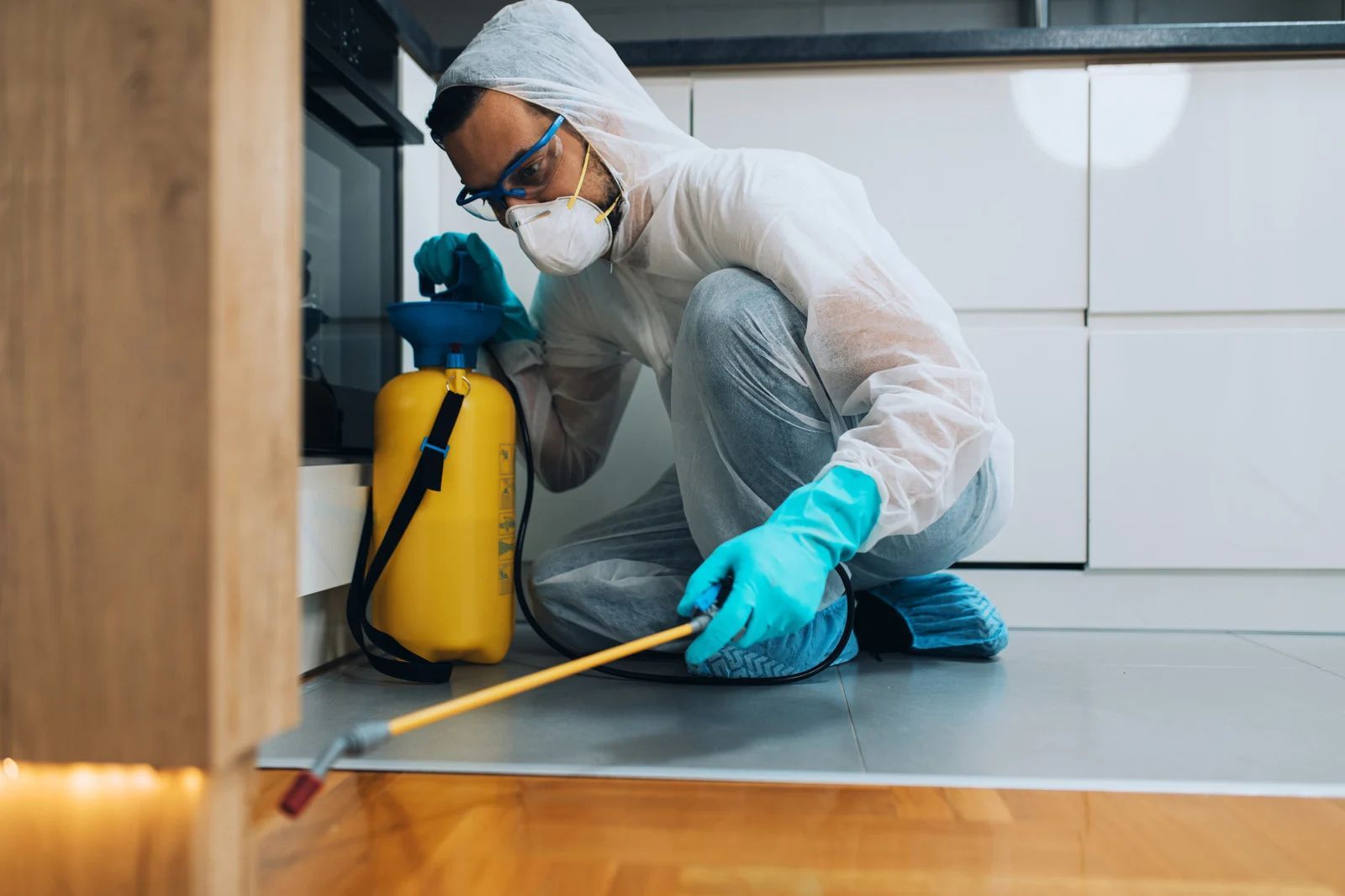 Person in protective gear sprays insecticide in a kitchen.
