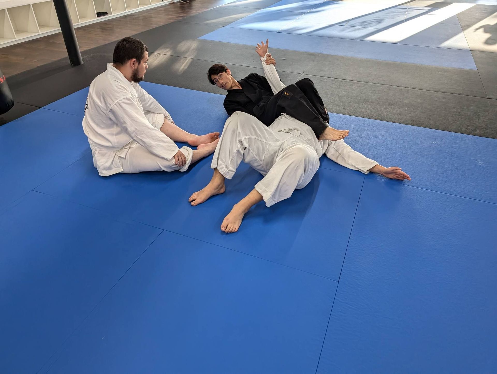 Two men are sitting on a blue mat in a gym.