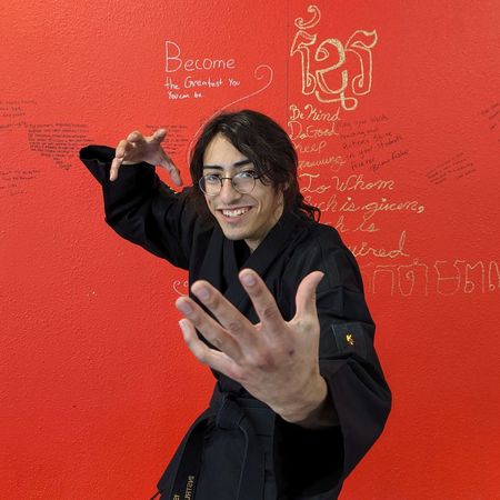 A man in a black karate uniform is standing in front of a red wall that has become written on it