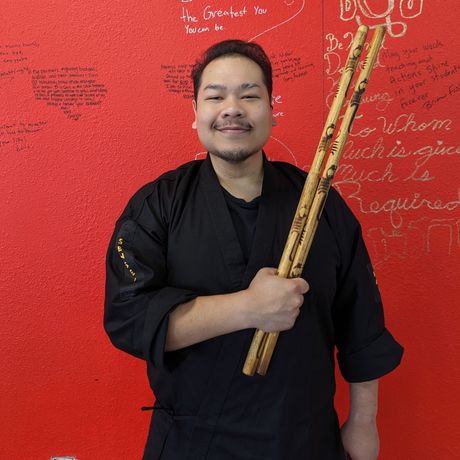 A man holding a wooden stick in front of a red wall