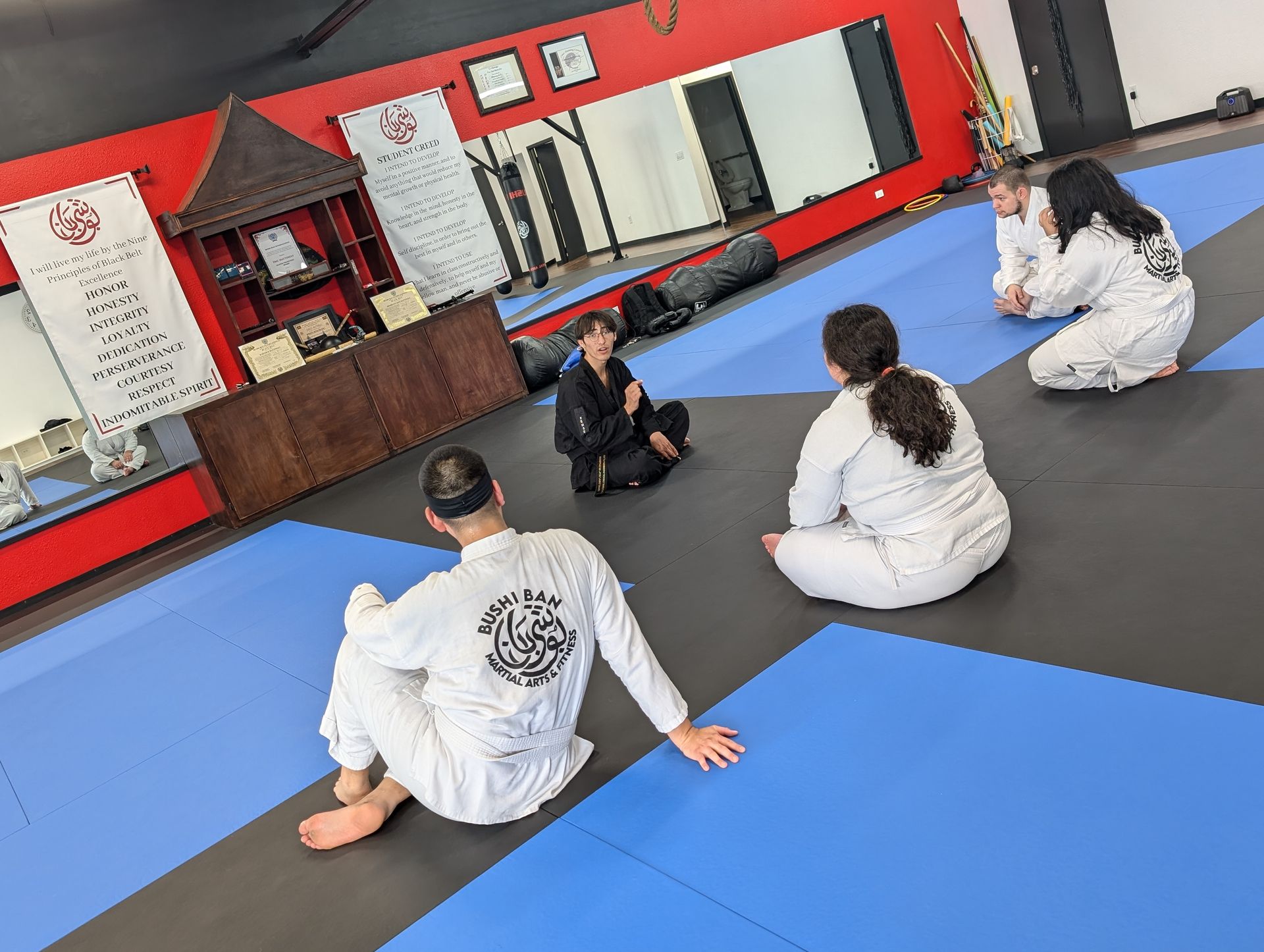 A group of people are sitting on a blue mat in a gym.