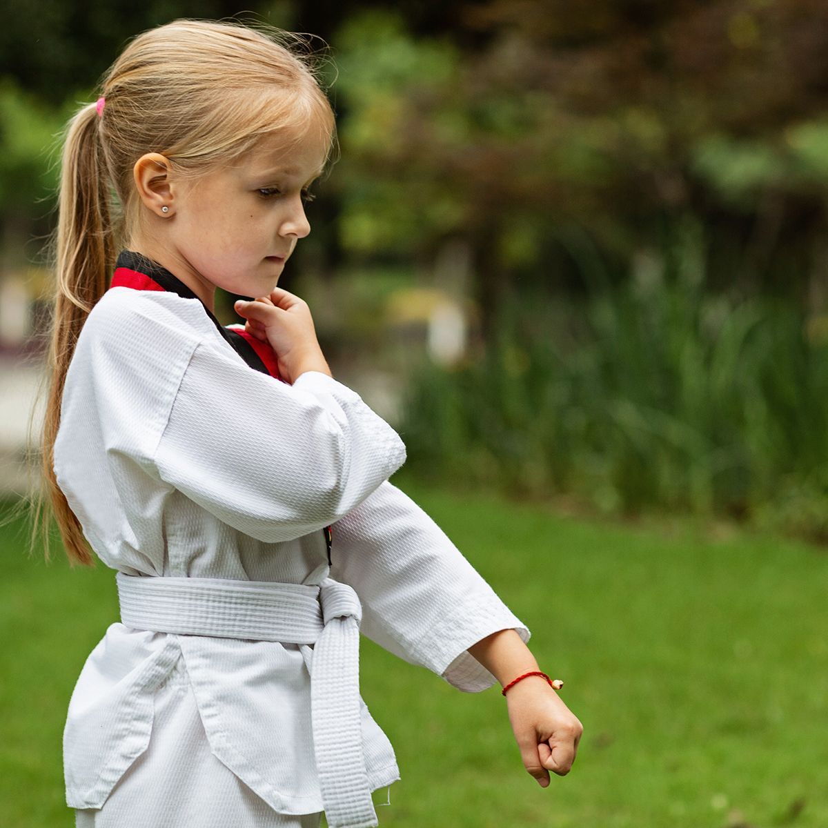 A little girl in a white karate uniform is standing in the grass.