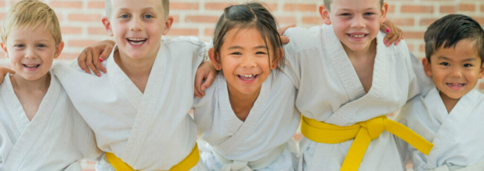 Karate kids standing with arms around each other laughing.