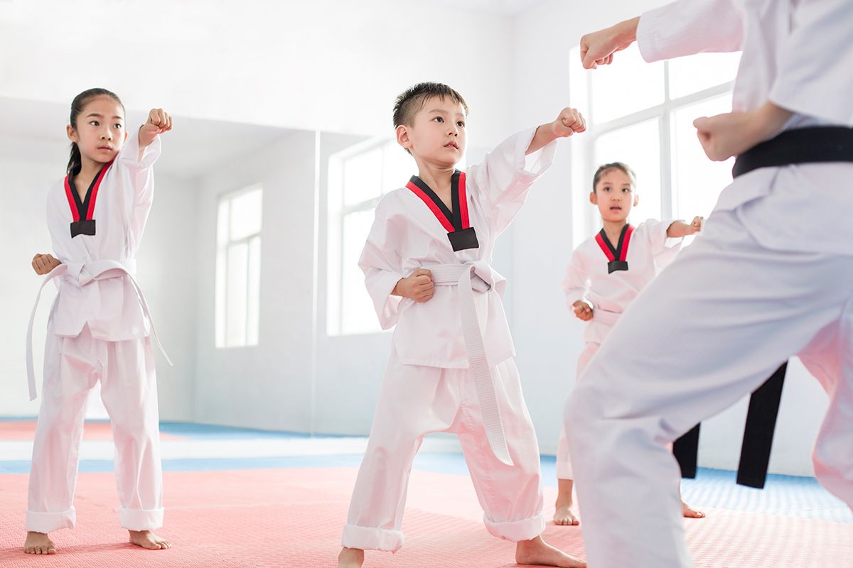 A group of children are practicing karate with a teacher in a gym.