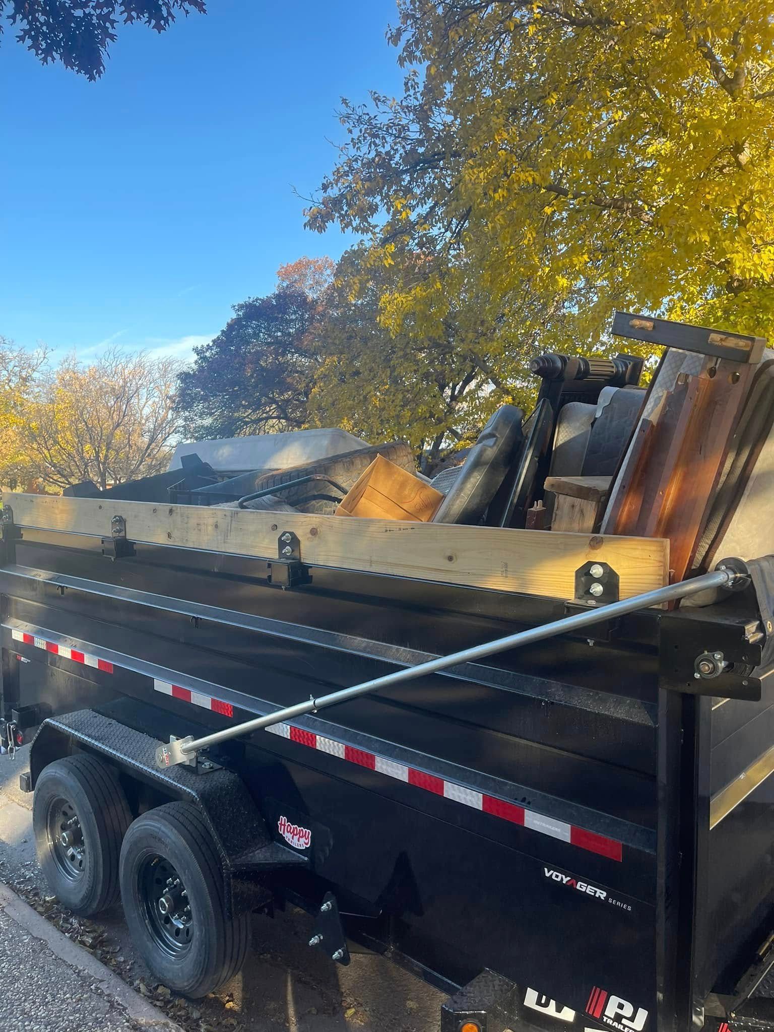 A dumpster is sitting on the side of the road next to a tree.