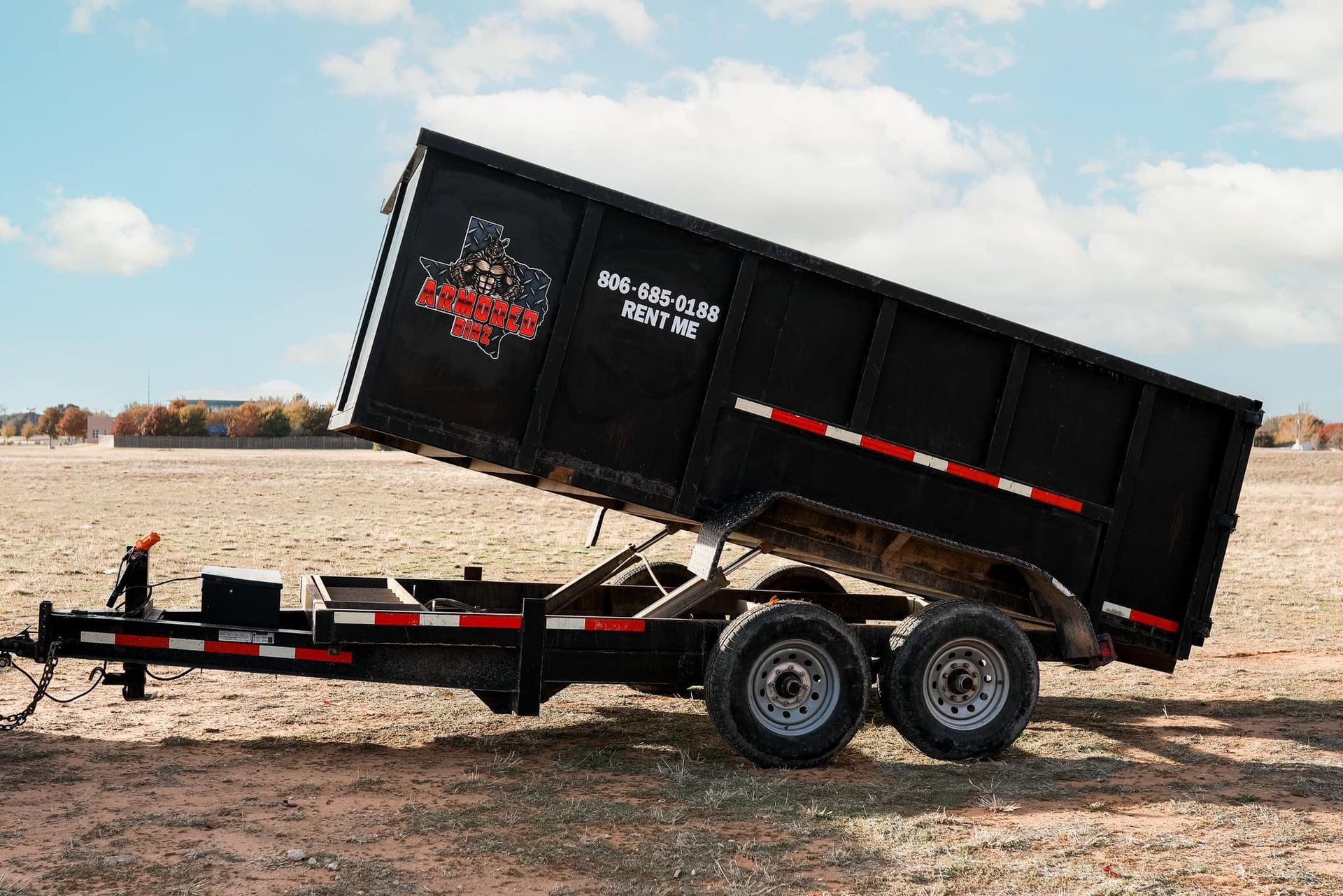A dumpster trailer is parked in the middle of a dirt field.