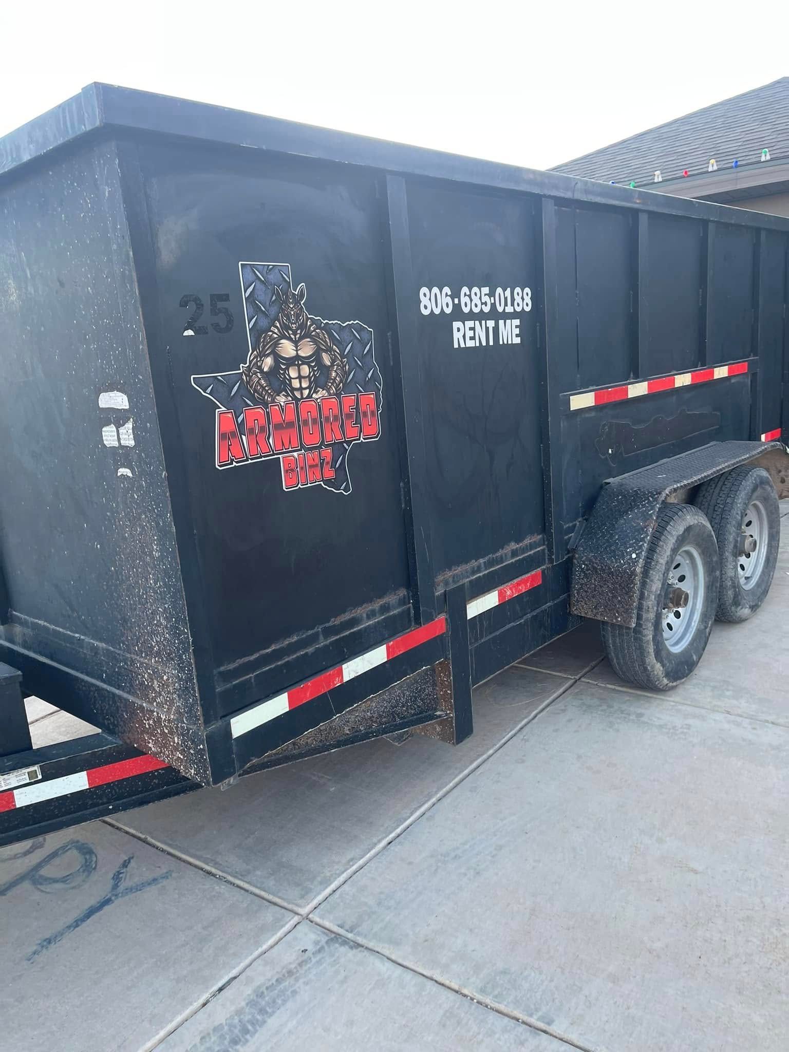 A black dumpster trailer is parked on the side of the road.