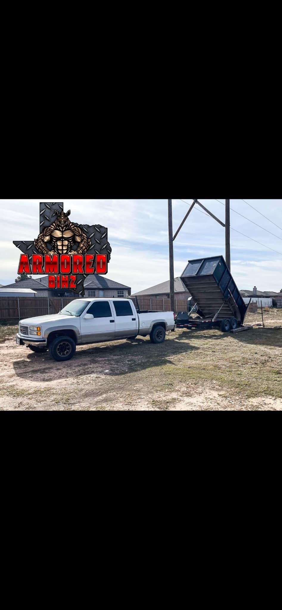 A white truck is towing a dumpster in a field.