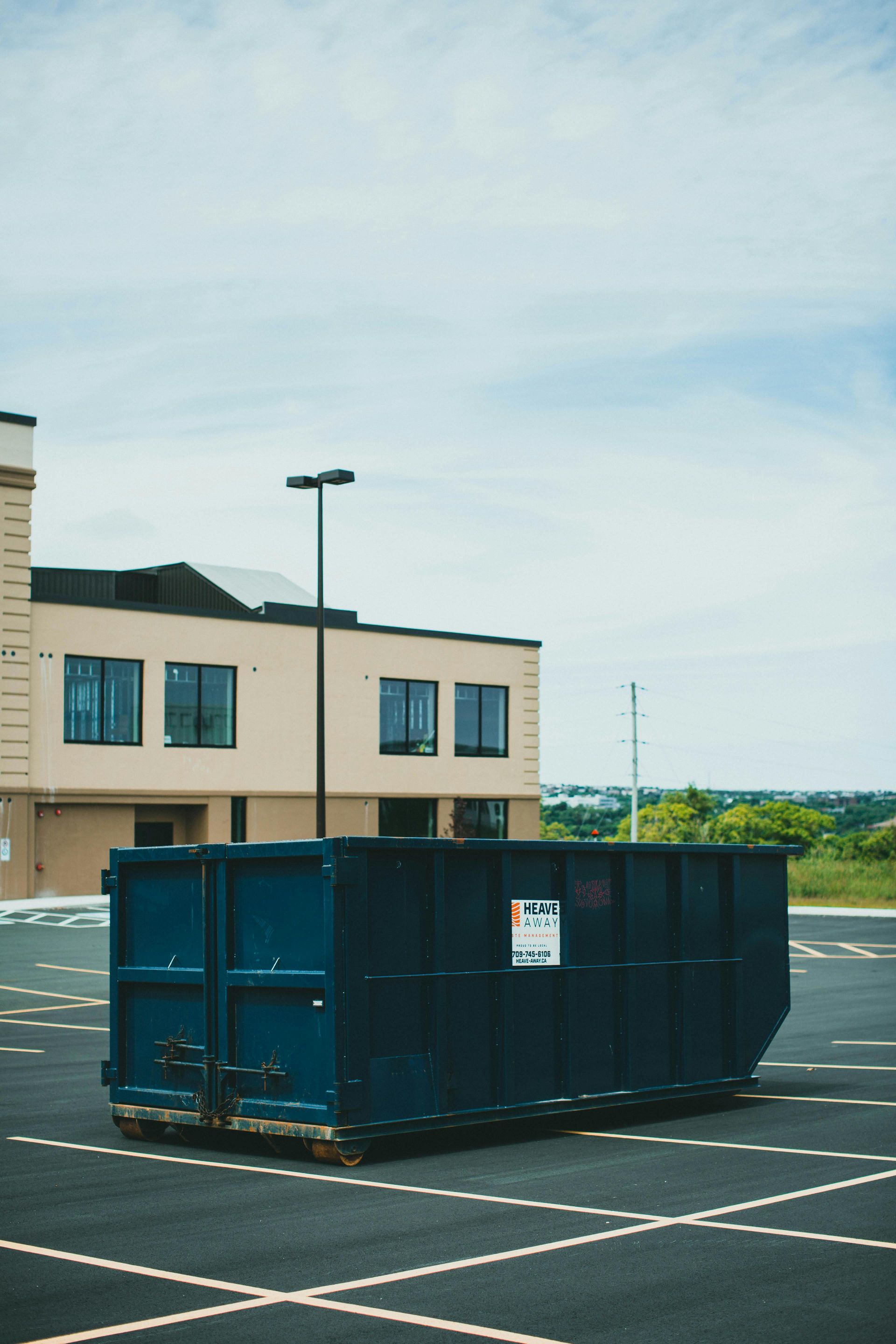 A blue dumpster is parked in a parking lot in front of a building