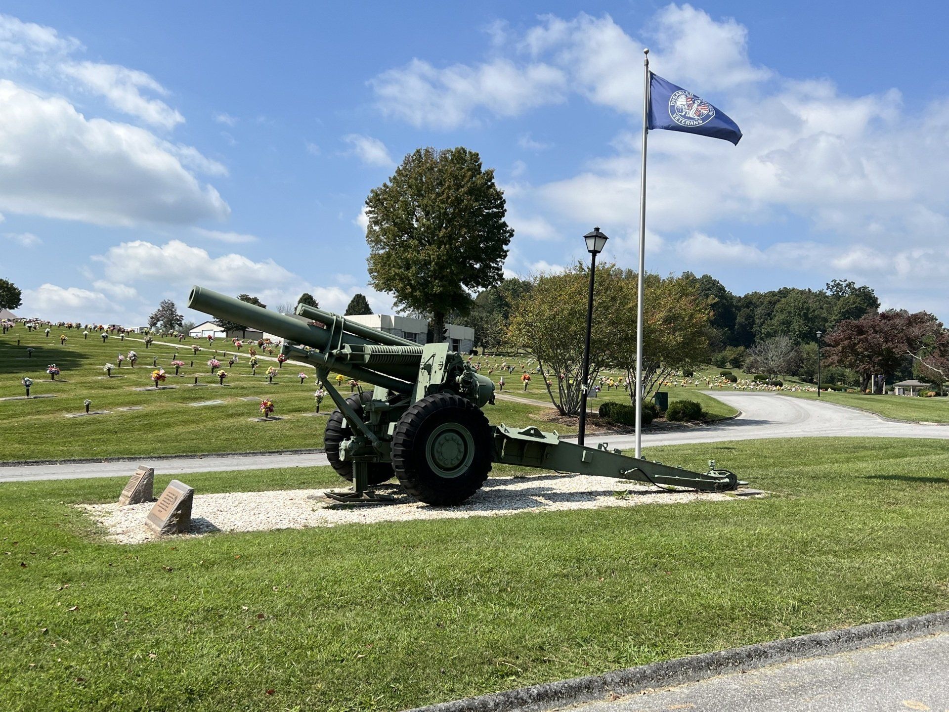 A cannon is sitting in the grass in front of a cemetery with a flag flying in the background.