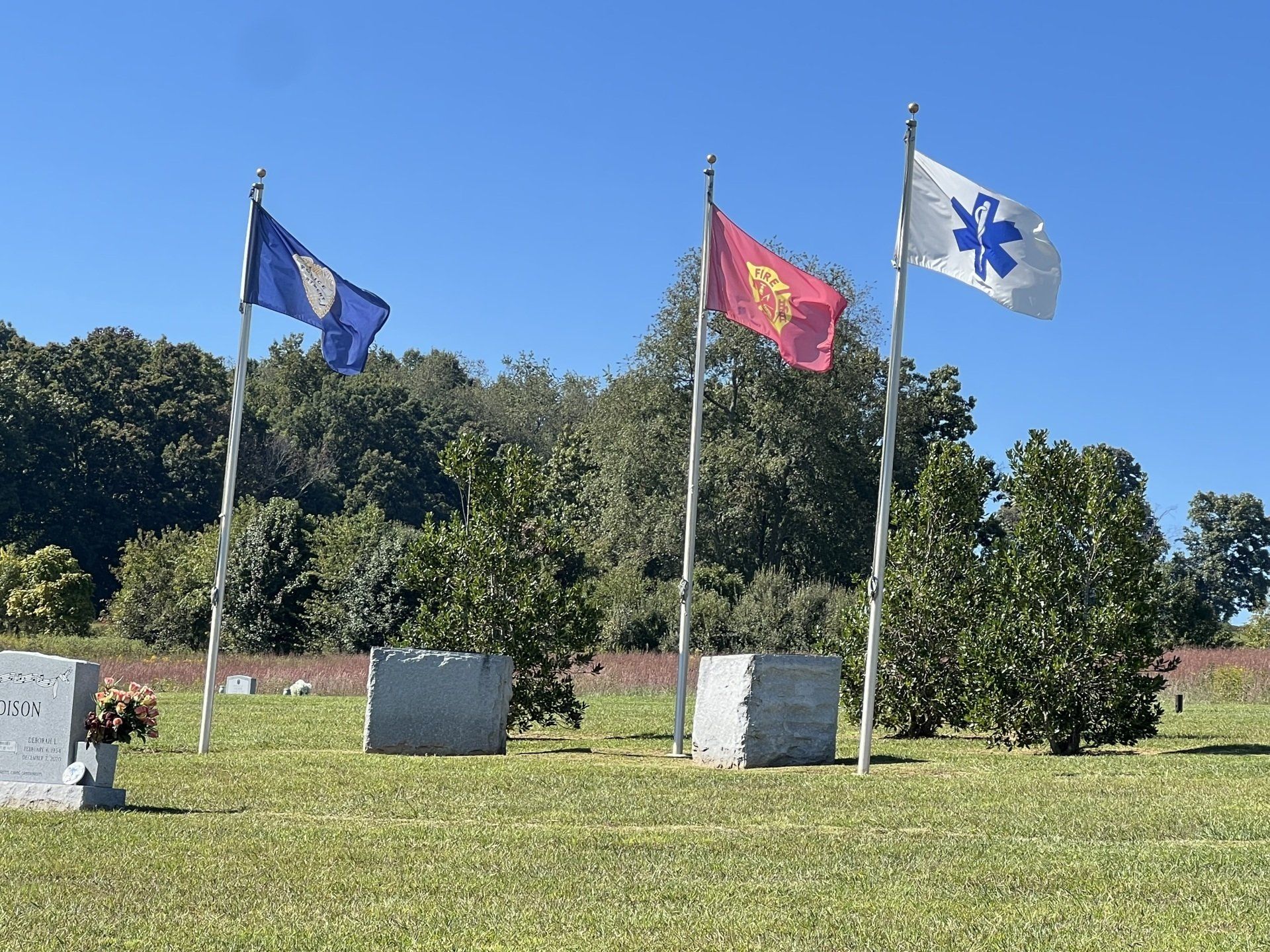 Three flags are flying in a cemetery with trees in the background