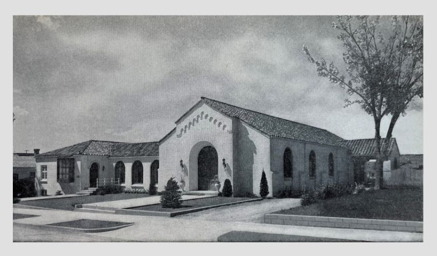 A black and white photo of a building with a tree in front of it