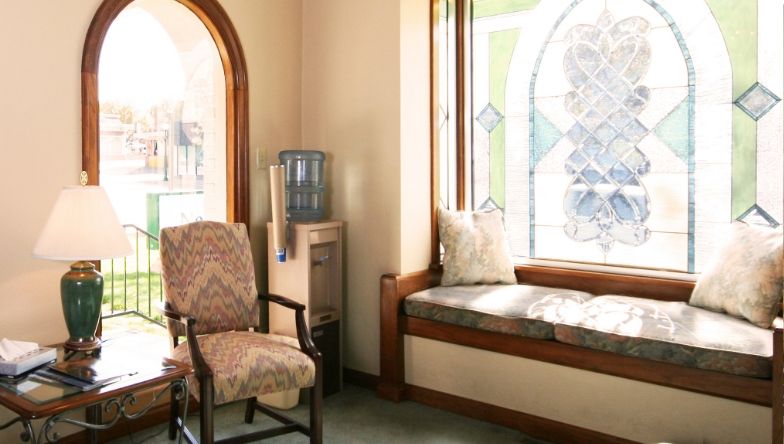 A waiting room with chairs , a table and a stained glass window.