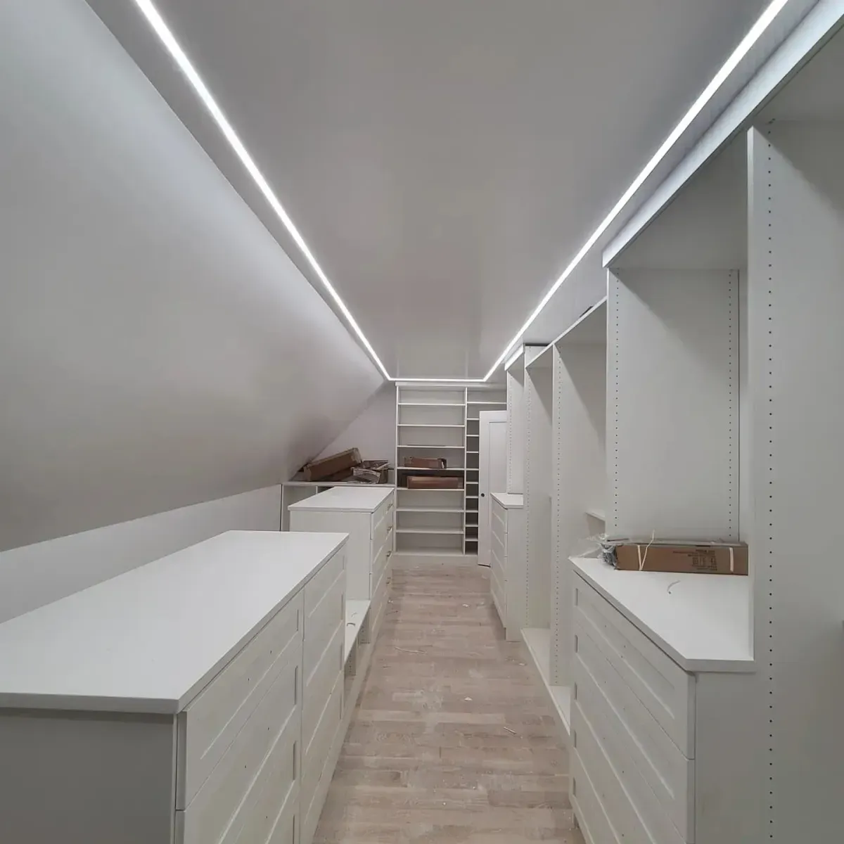 A walk in closet with lots of white dressers and shelves