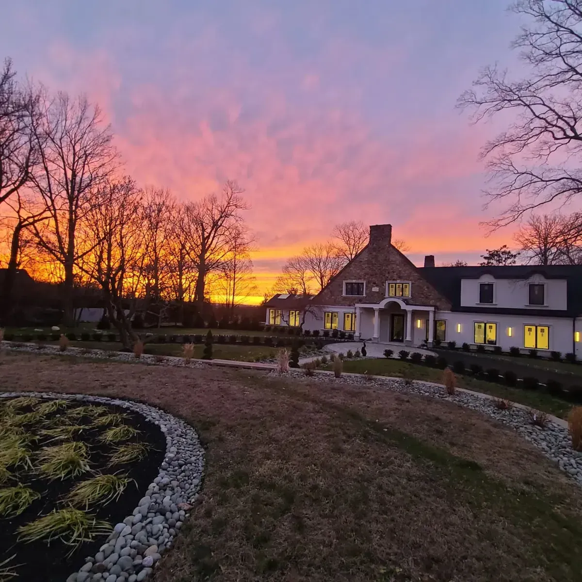A house with a sunset in the background and trees in the foreground.