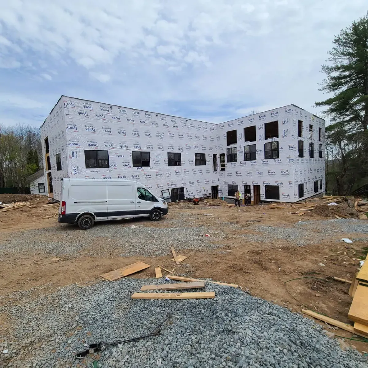A white van is parked in front of a large building under construction.