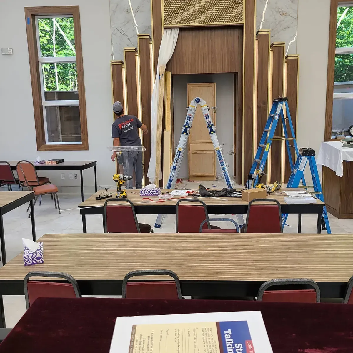 A man is standing in a room with tables and chairs and a ladder
