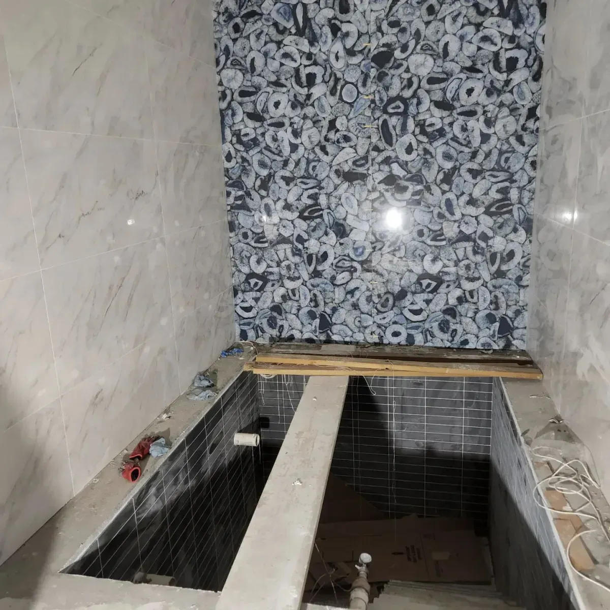 A bathtub is being built in a bathroom with a tiled wall.