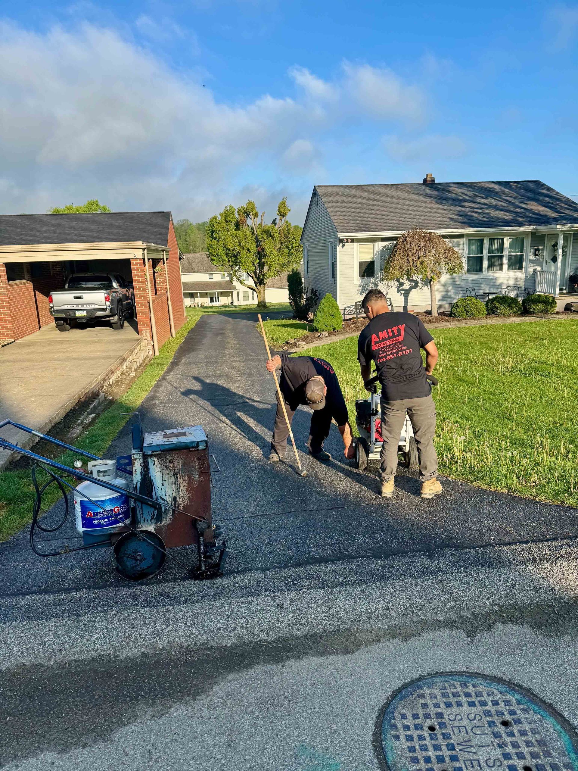 Two men are working on a driveway in front of a house.