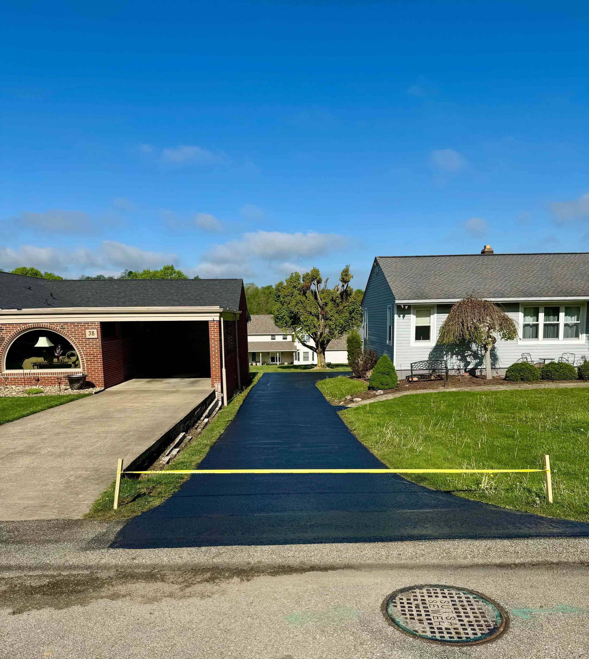 A person is spreading asphalt on a sidewalk with a broom.