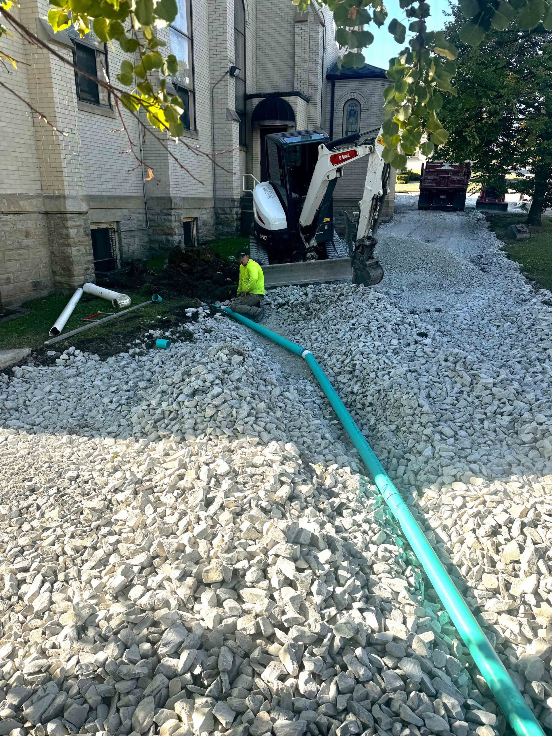 A man is standing in a pile of gravel next to a green hose.