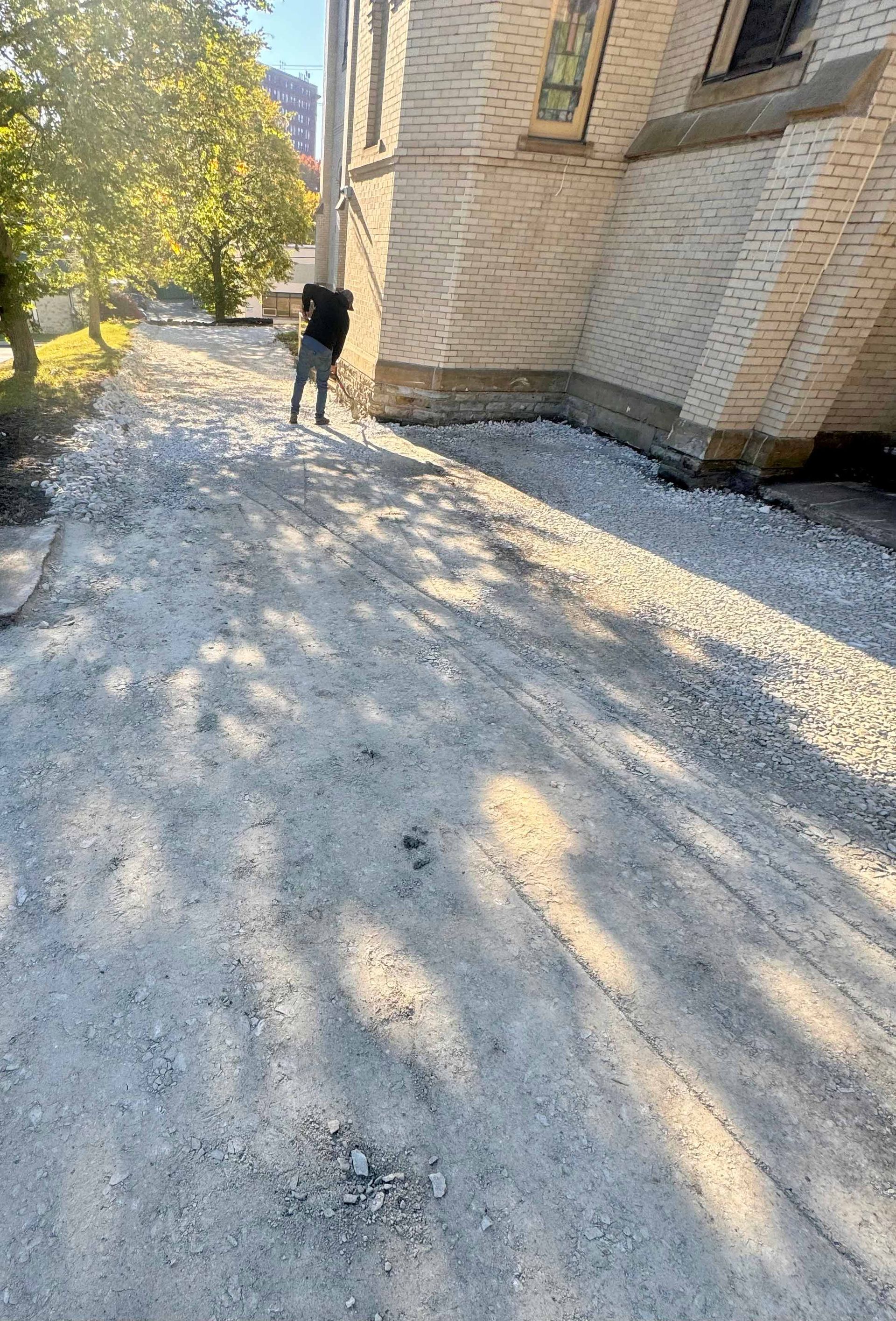 A person is standing on a dirt road in front of a building.
