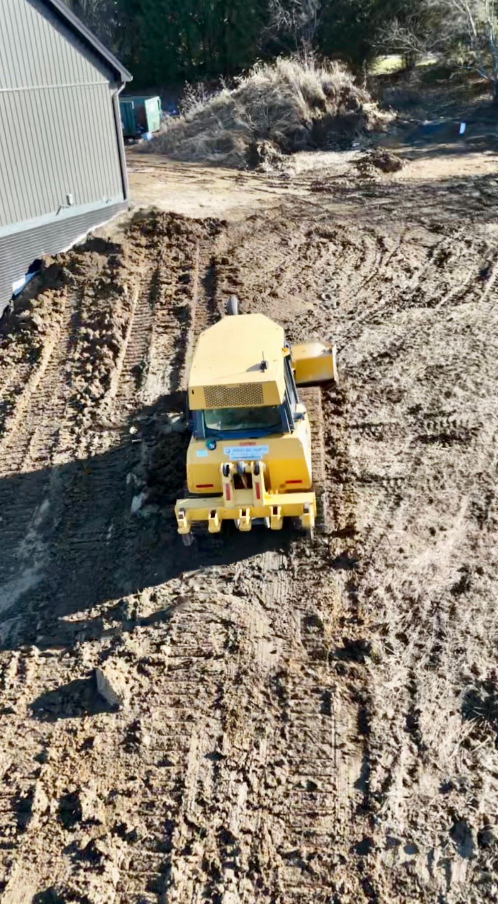 A yellow excavator is working on a construction site with a crane in the background.