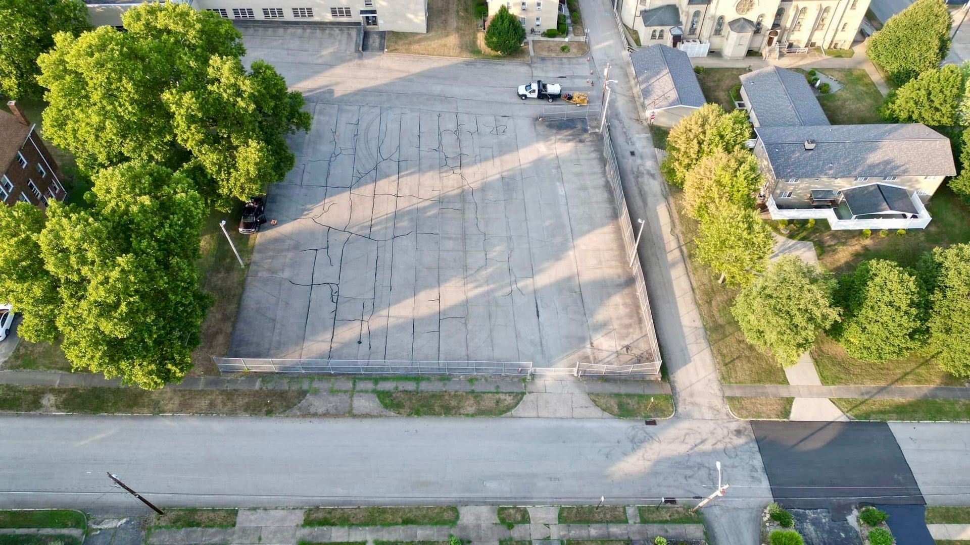 Before an aerial view of a parking lot surrounded by trees and buildings.