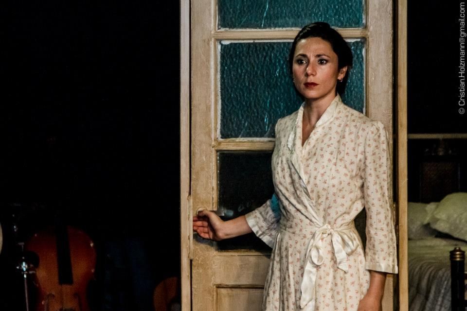 Mujer con túnica floral sosteniendo una puerta abierta, entorno de dormitorio.