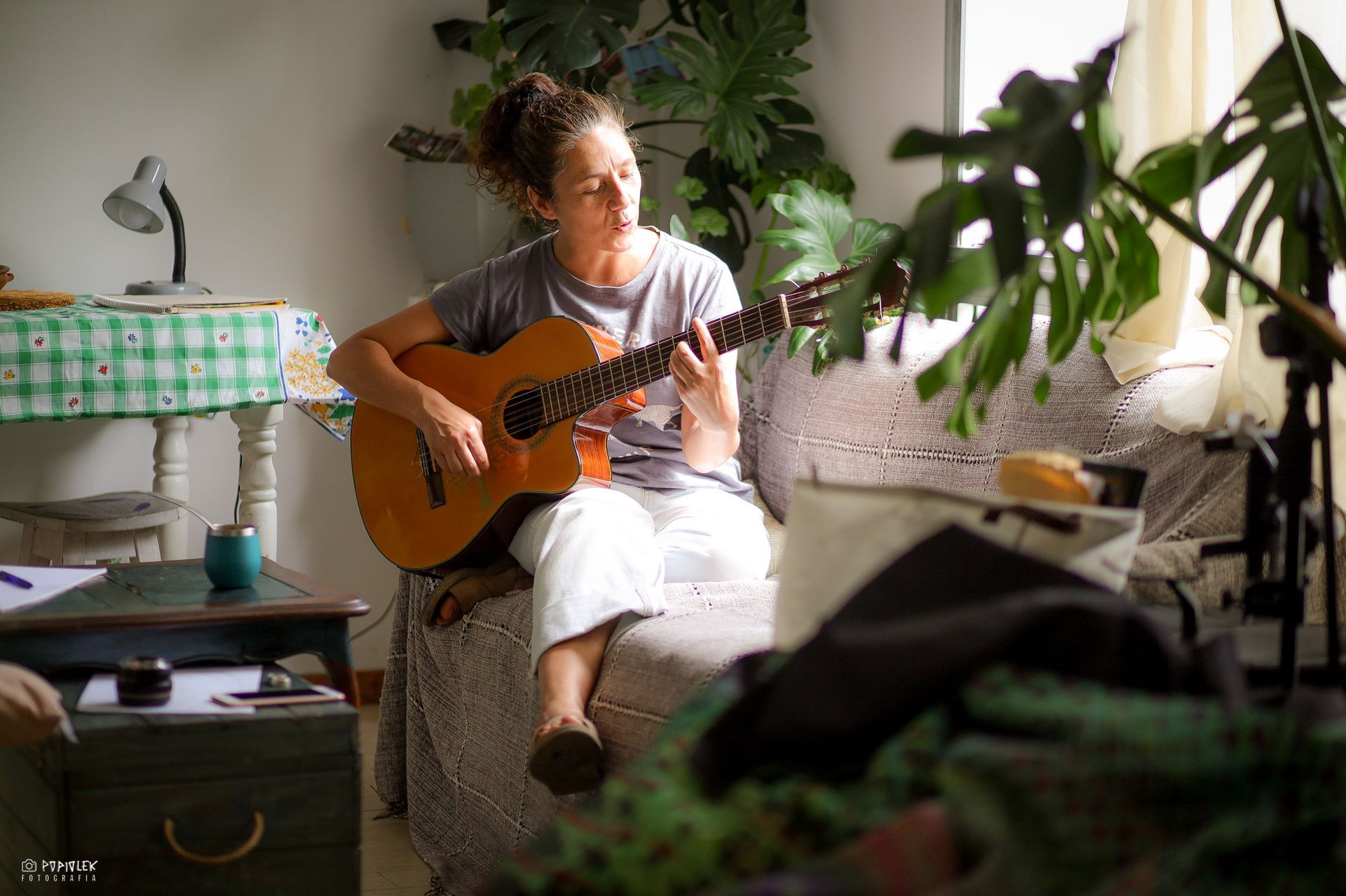 Mujer sentada, tocando la guitarra acústica en un interior con luz natural.