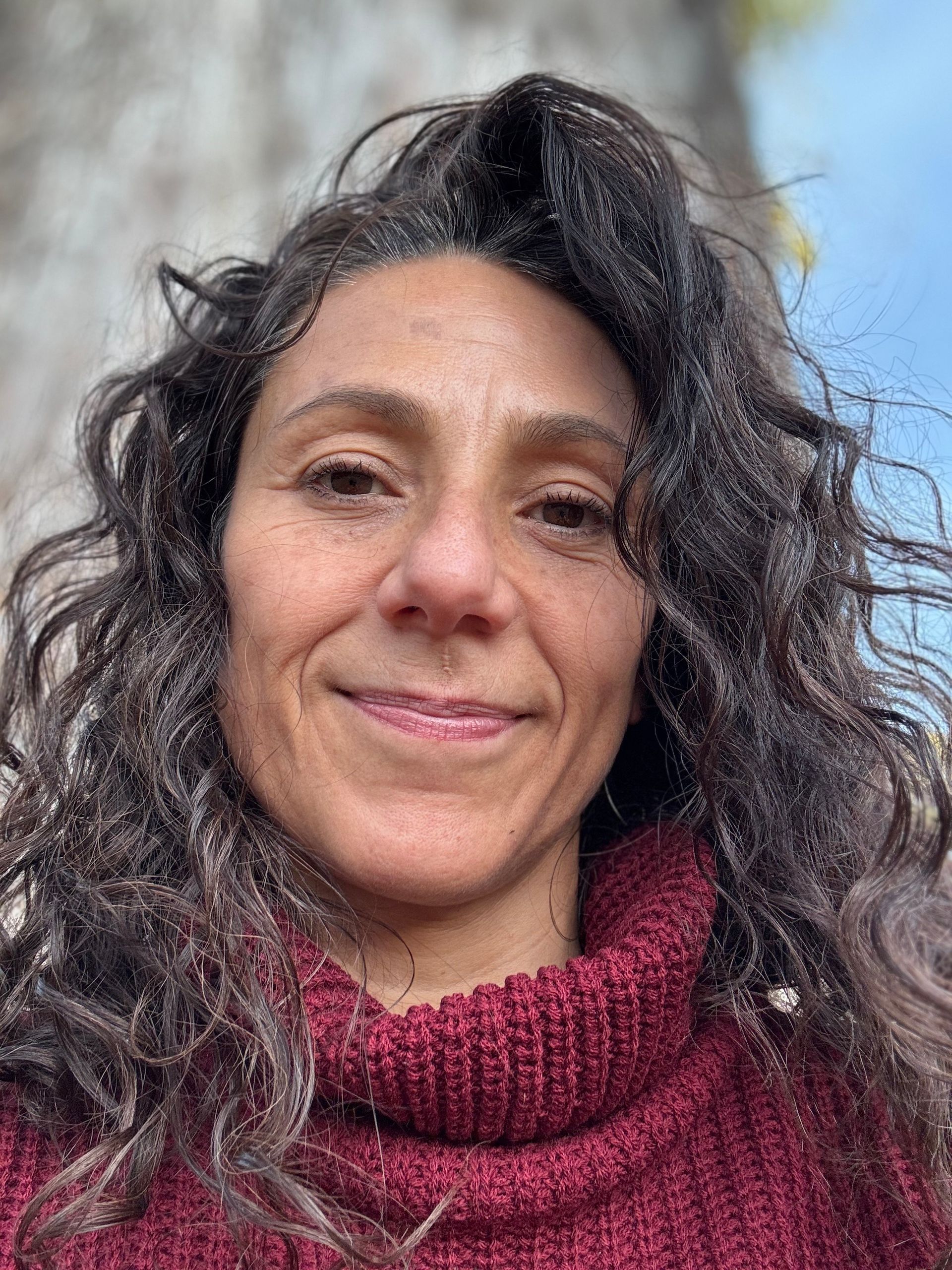 Una mujer con cabello rizado lleva un suéter rojo y sonríe.