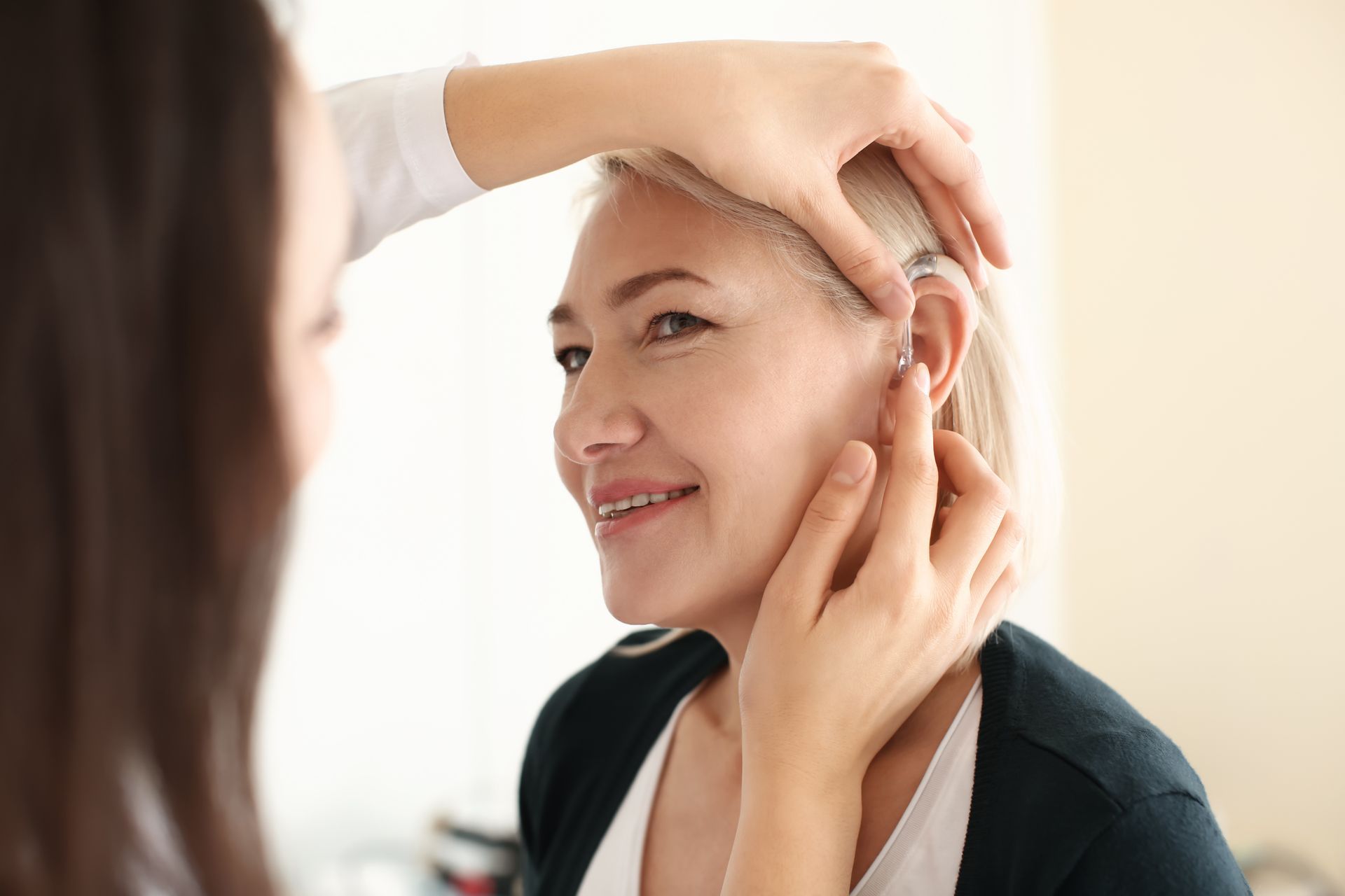 Professional audiologist fitting a digital hearing aid for a smiling senior woman in a clinic.
