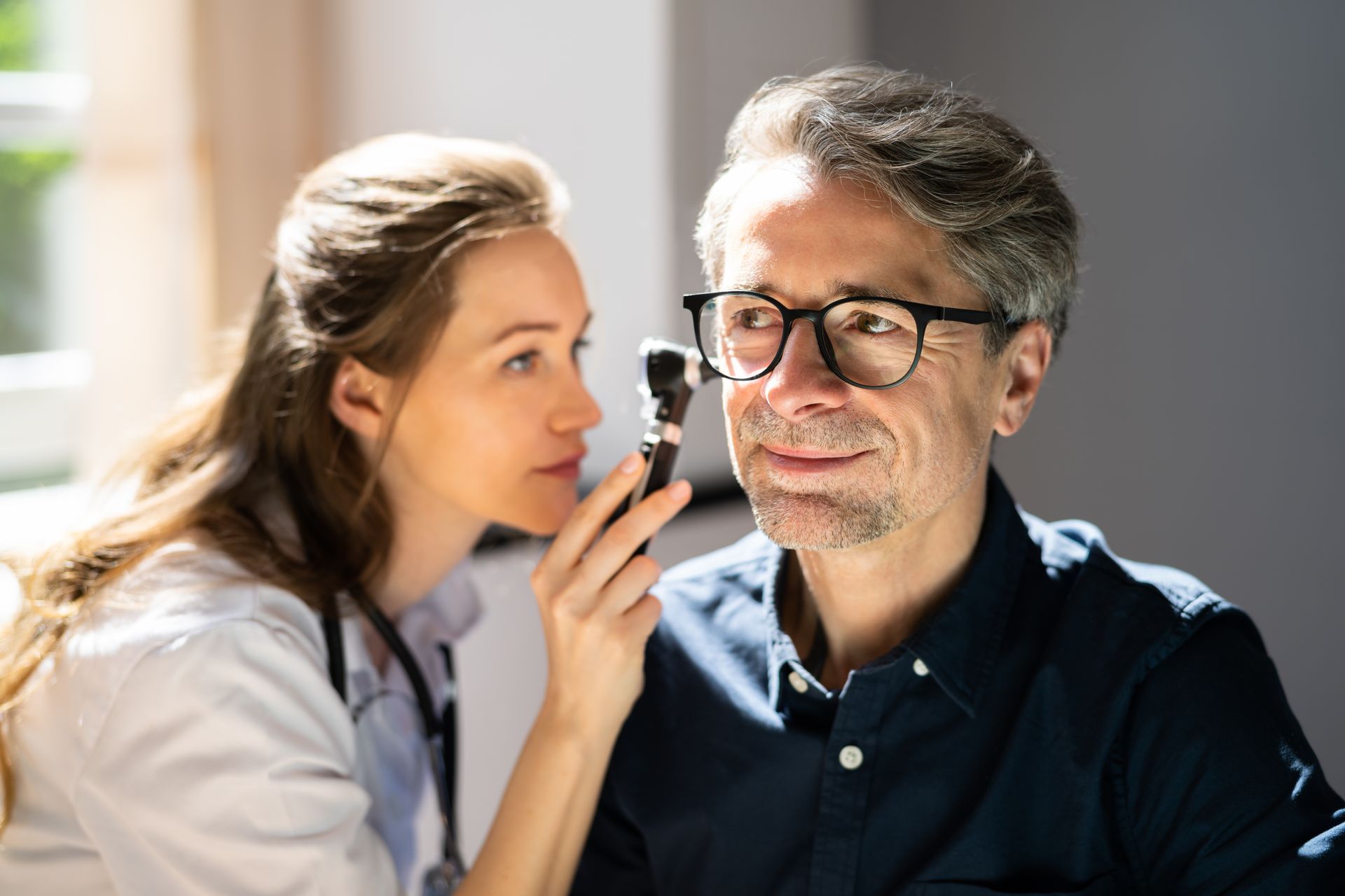 A female audiologist using an otoscope to perform a professional ear exam on a senior male patient.
