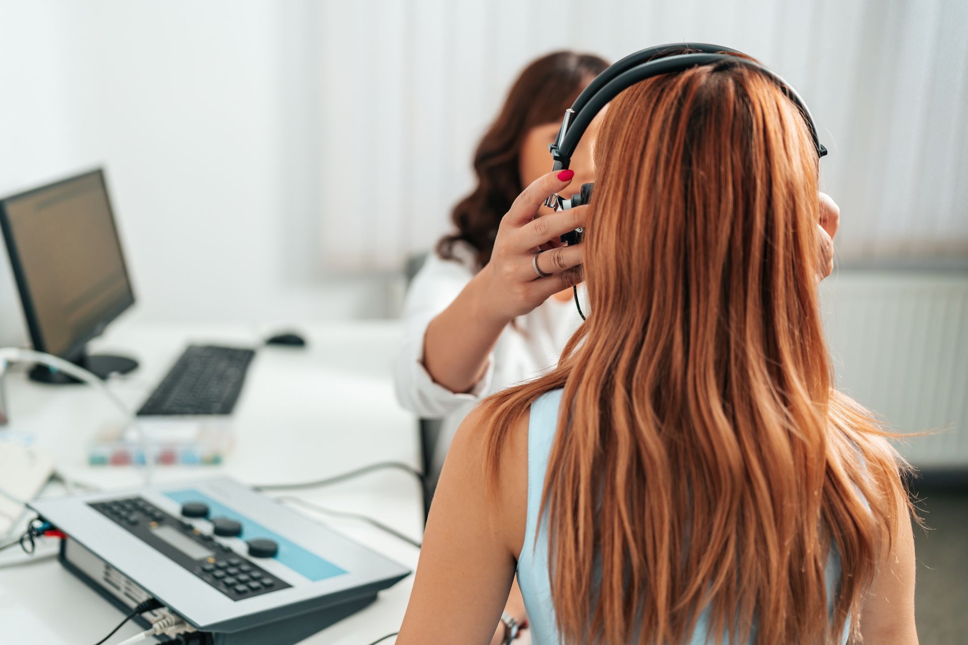 Hearing test in progress as a clinician adjusts headphones on a patient in an exam room.