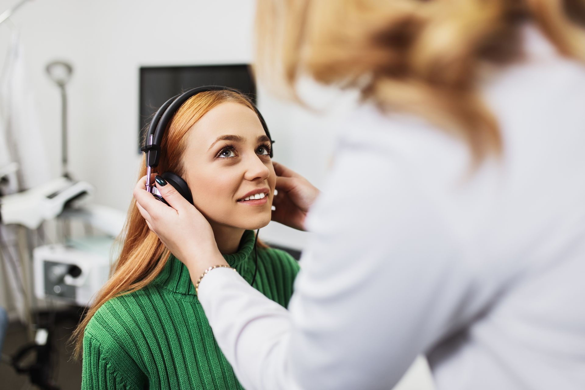 Woman in green sweater getting hearing test with headphones by a medical professional.