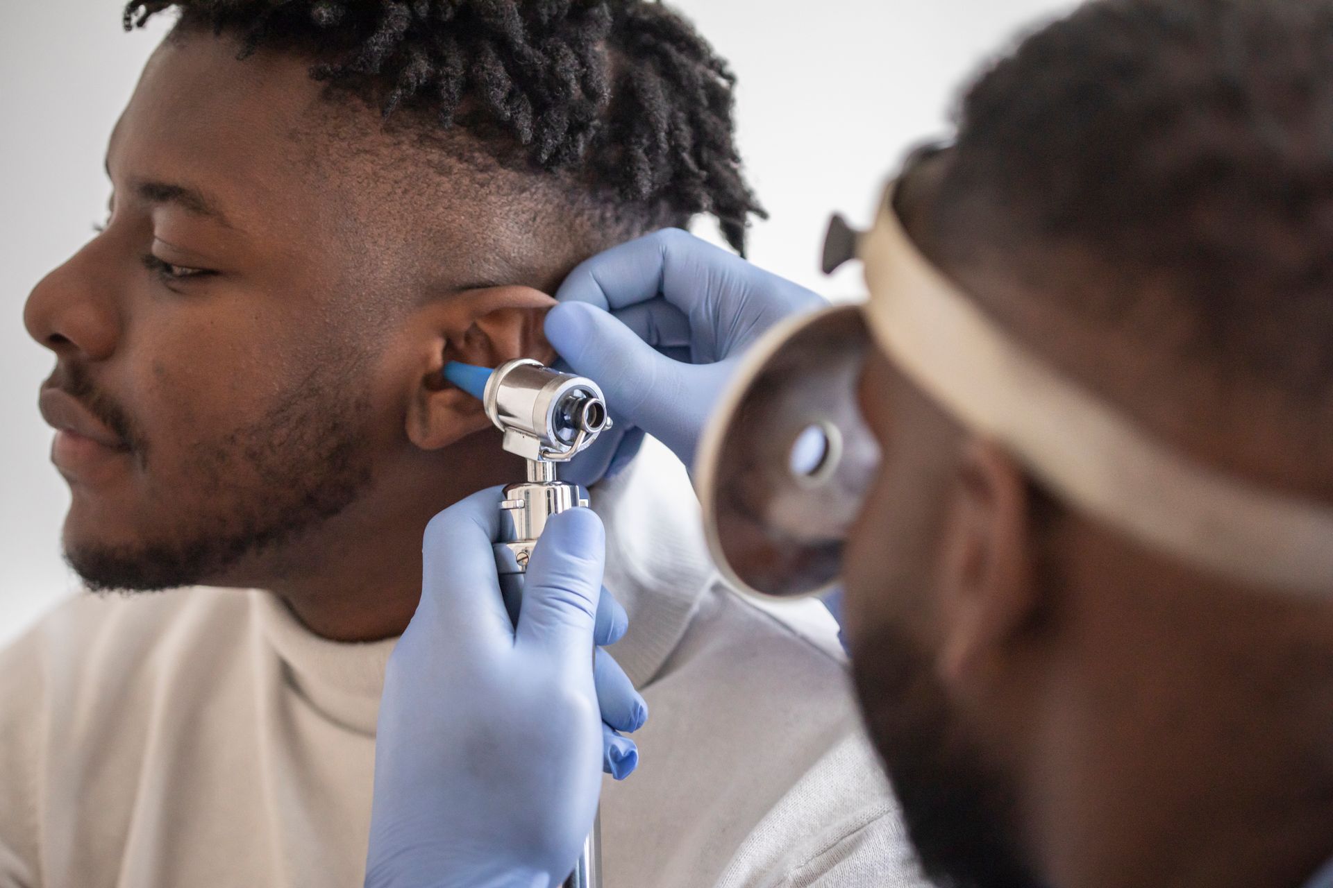 A doctor examines a Black man's ear with an otoscope in a brightly lit room.