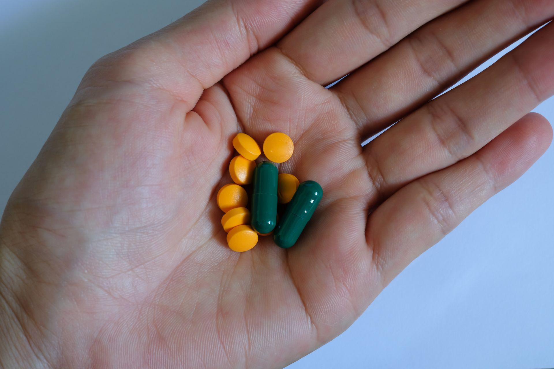 Hand holding a mix of orange pills and green capsules.
