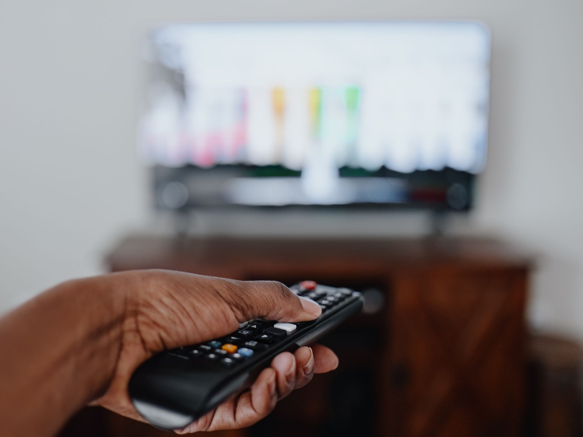 Hand holding a remote, pointing it at a TV displaying a colorful test pattern; indoors.
