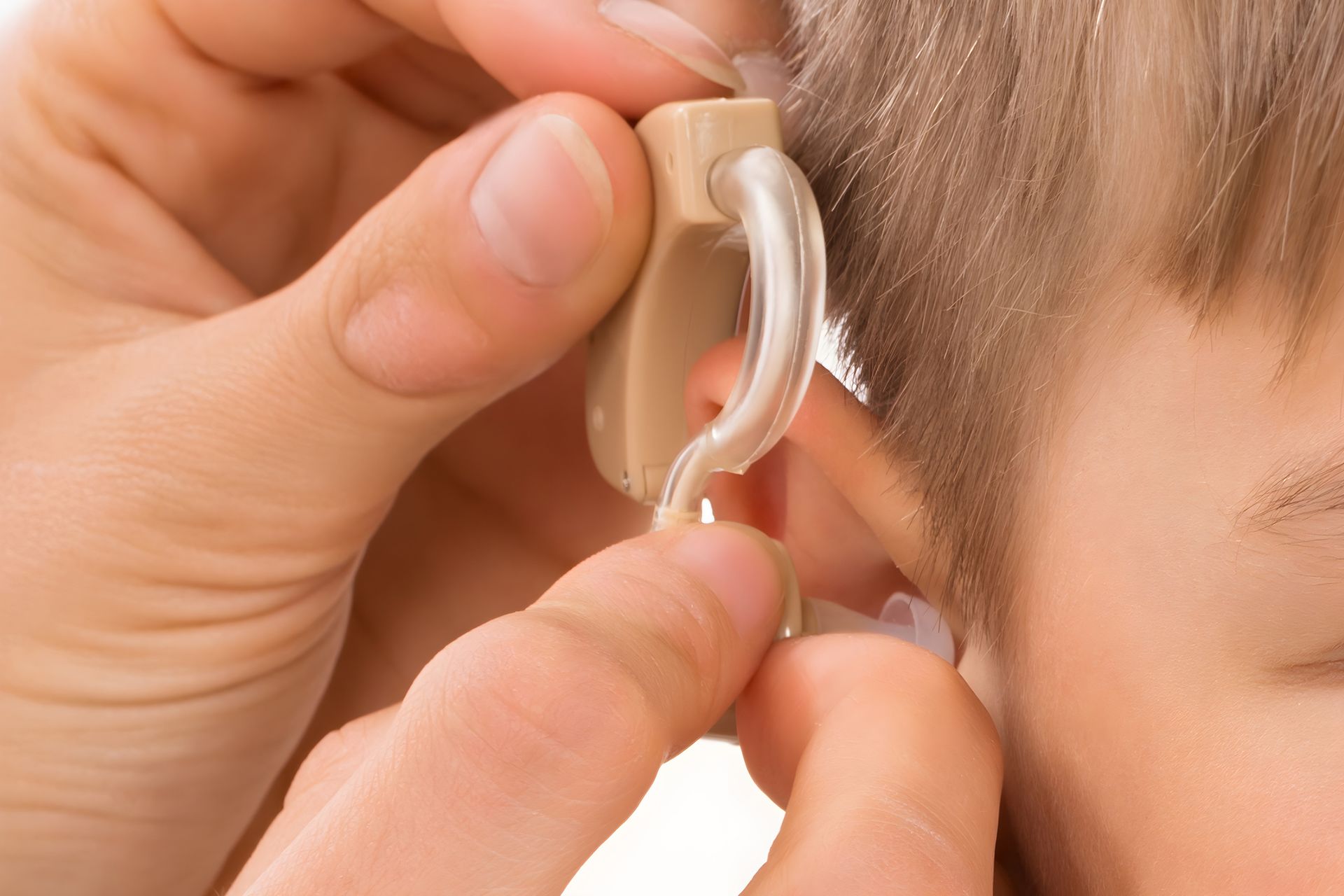 Person fitting a beige hearing aid into a child's ear. White skin, close-up.