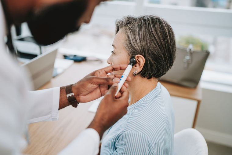 Doctor examining a woman's ear with an otoscope in a bright office setting.