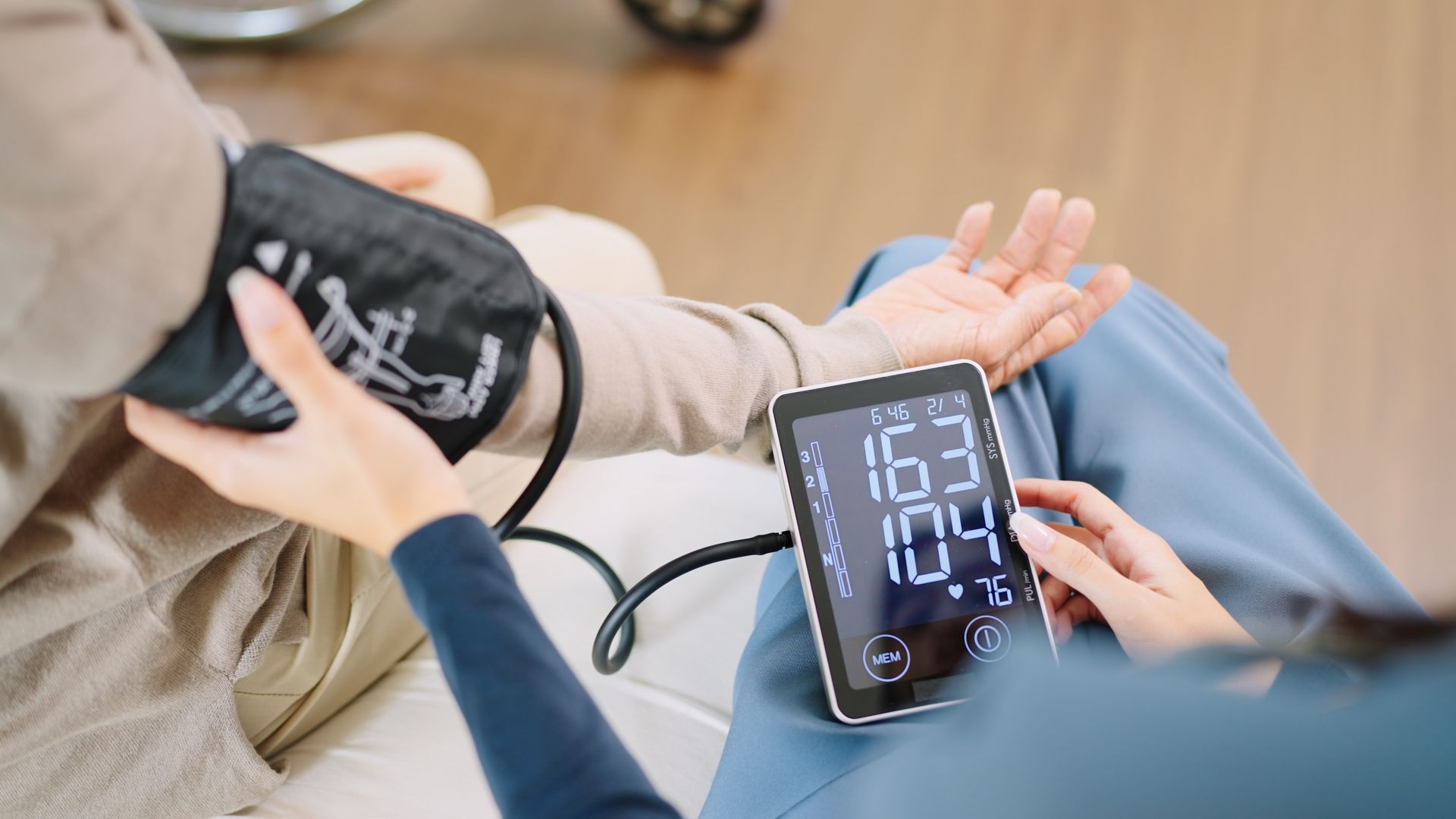 Person's blood pressure is taken with a digital monitor. A healthcare worker wraps cuff on arm. Screen displays 163/109.