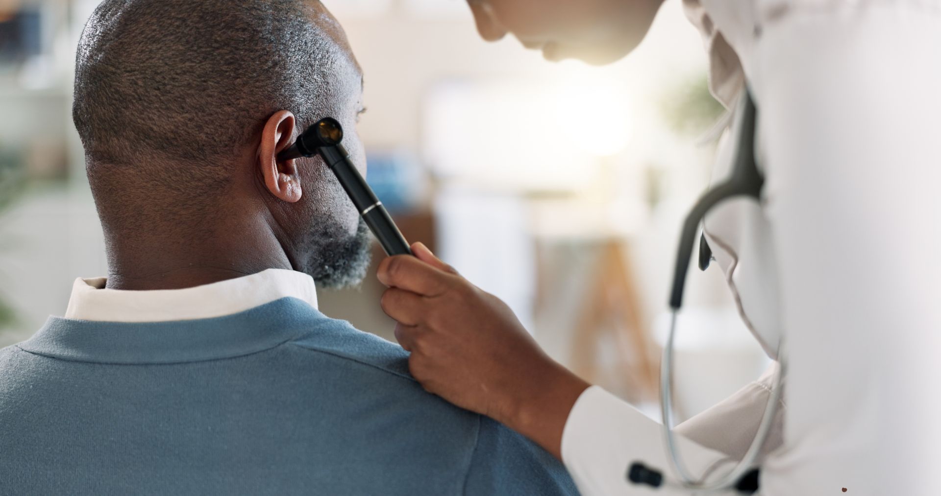 Doctor examining patient's ear with otoscope; clinic setting.