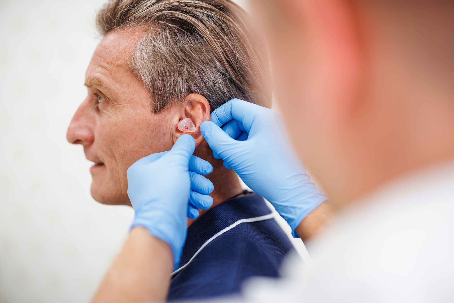 Man getting a hearing aid fitted by someone wearing blue gloves.